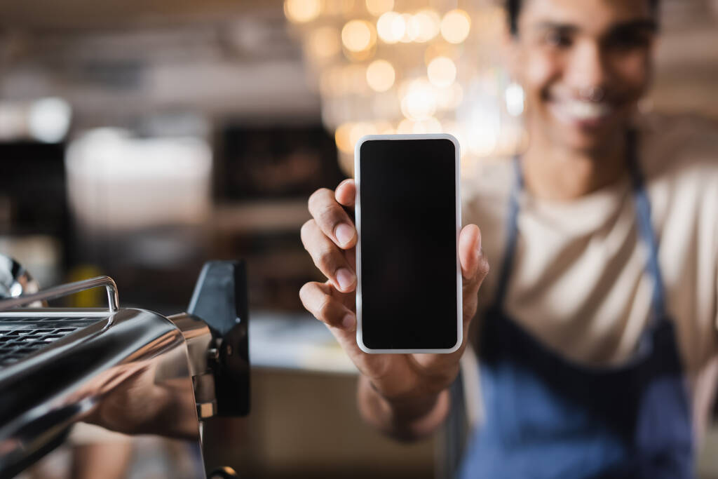 Smartphone met blanco scherm in de hand van wazig Afrikaans Amerikaans barista in cafe - Foto, afbeelding