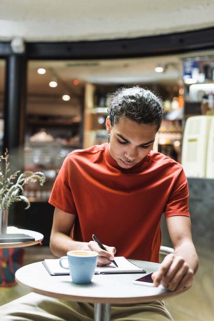Hombre afroamericano escribiendo en portátil cerca de café y teléfono inteligente en la cafetería  - Foto, imagen