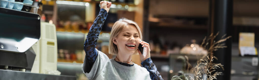 Mujer rubia emocionada hablando en el teléfono inteligente en la cafetería, pancarta  - Foto, imagen
