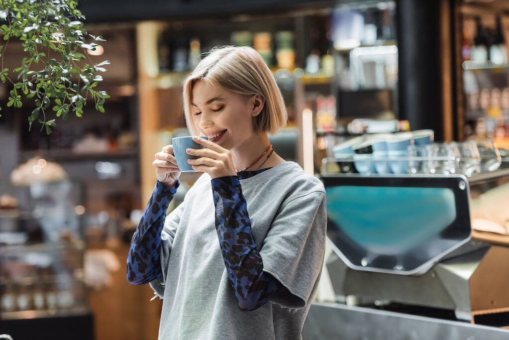Позитивная женщина с закрытыми глазами держит чашку в кафе - Фото, изображение