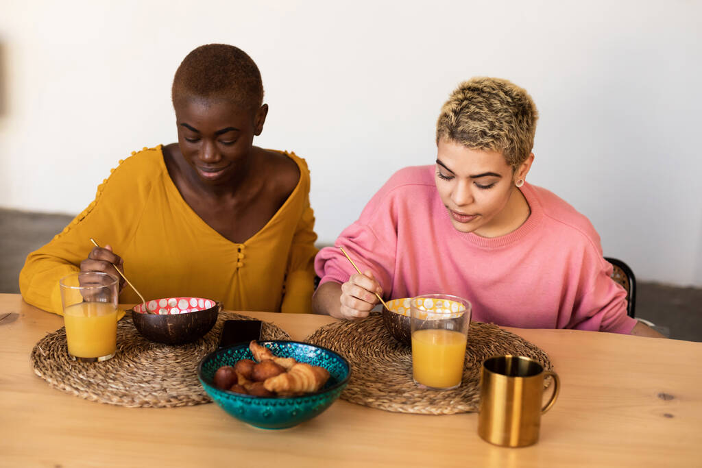 Feliz casal feminino multiétnico relaxando em casa enquanto toma café da manhã - Foto, Imagem