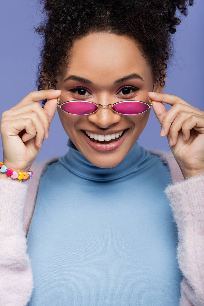 happy african american woman adjusting stylish sunglasses isolated on violet  - Photo, Image