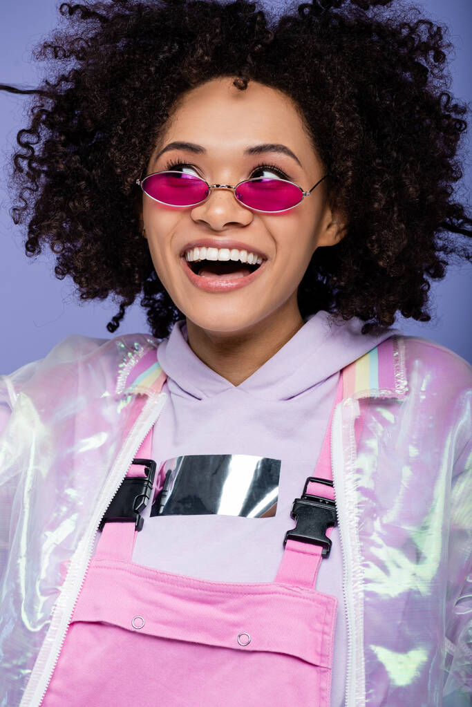 fröhliche afrikanisch-amerikanische Frau mit Sonnenbrille schaut vereinzelt auf lila - Foto, Bild