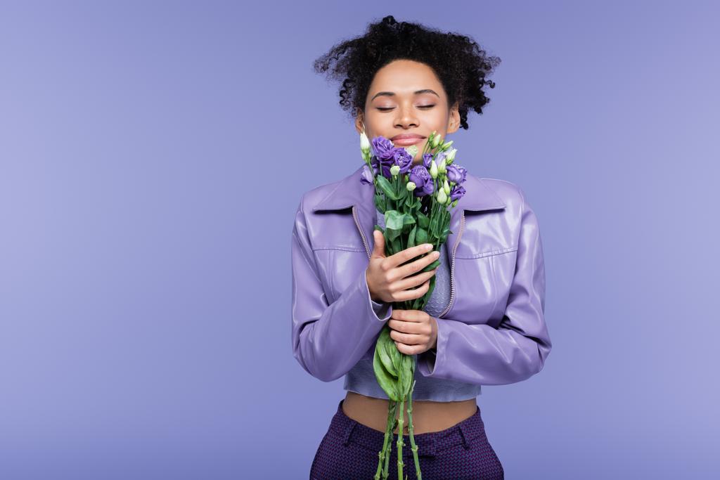 Memnun genç Afro-Amerikalı kadın elinde buket ve mor üzerine izole edilmiş çiçekler tutuyor. - Fotoğraf, Görsel