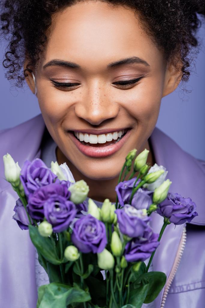 positivo giovane donna afroamericana guardando fiori viola sfocati isolati su viola - Foto, immagini