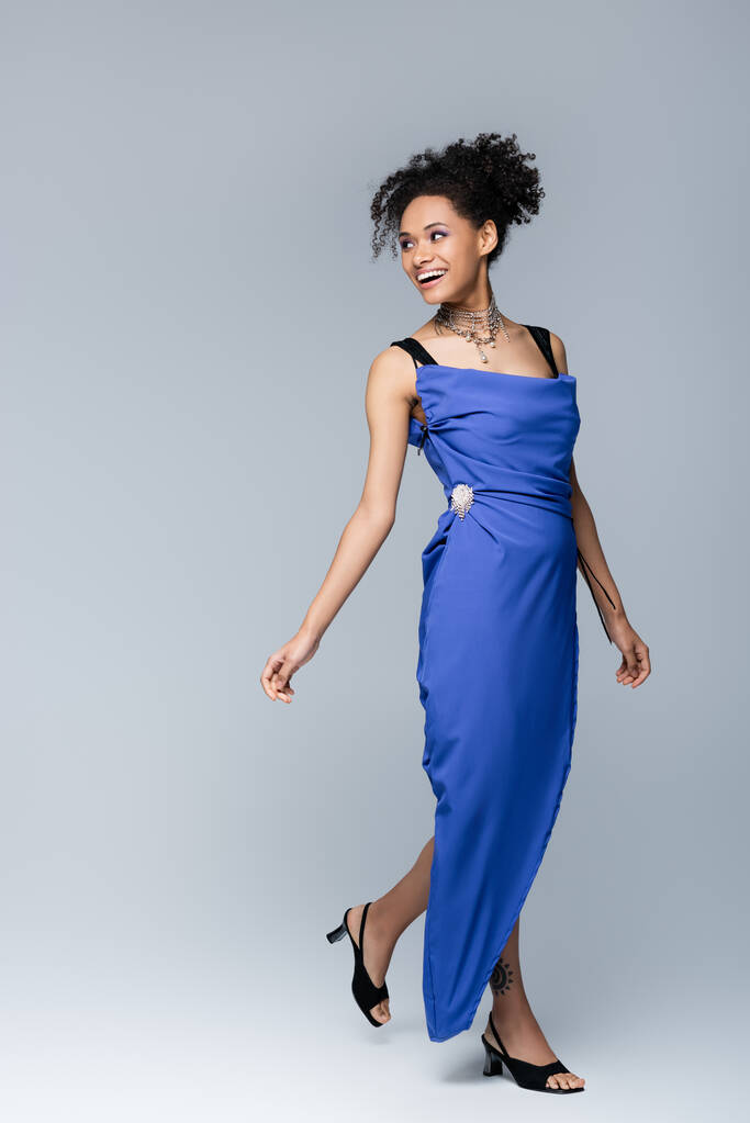 longitud completa de la mujer afroamericana feliz en vestido azul brillante en gris - Foto, imagen