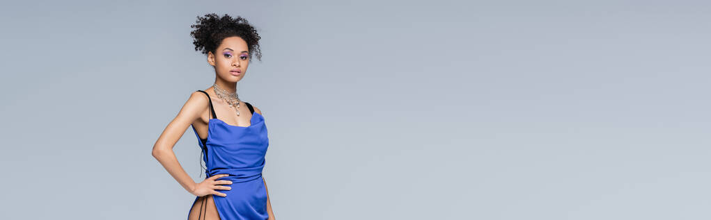élégante femme afro-américaine en robe bleu vif posant à la main sur la hanche isolée sur gris, bannière - Photo, image
