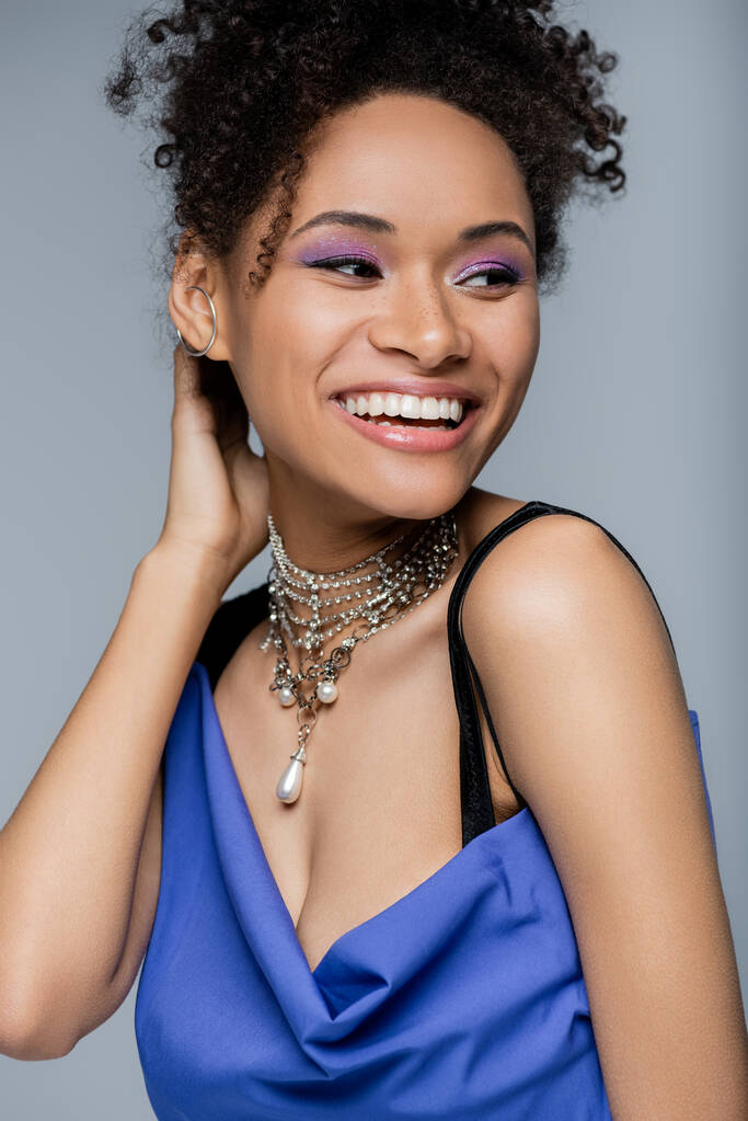 szczęśliwa Afroamerykanka z fioletowym cieniem do powiek uśmiechnięta na szaro - Zdjęcie, obraz