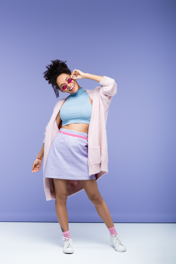 pleine longueur de femme afro-américaine positive ajuster les lunettes de soleil à la mode sur violet  - Photo, image