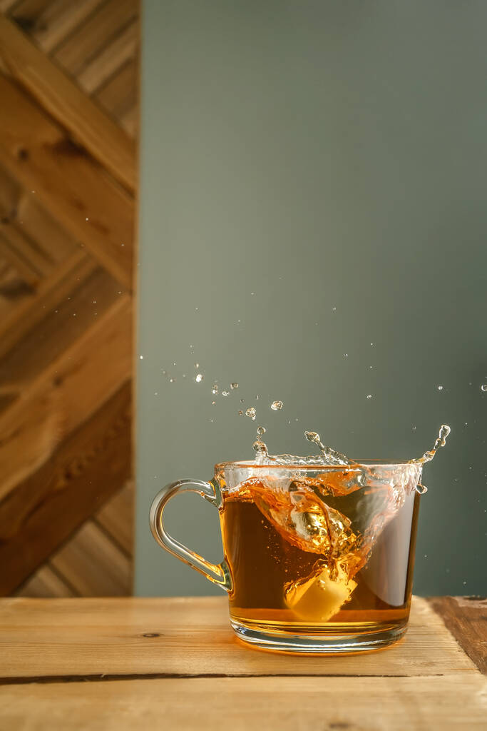 Průhledný hrnek s čajem a šploucháním na zeleném pozadí. - Fotografie, Obrázek