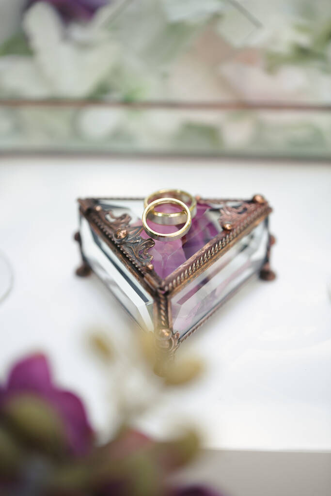 Svatební prsteny ve skleněné krabici s fialovými okvětními lístky růží. - Fotografie, Obrázek