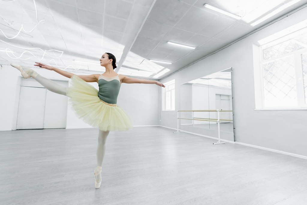 volledige weergave van slanke vrouw in tutu dansen met uitgestrekte handen in ballet studio - Foto, afbeelding
