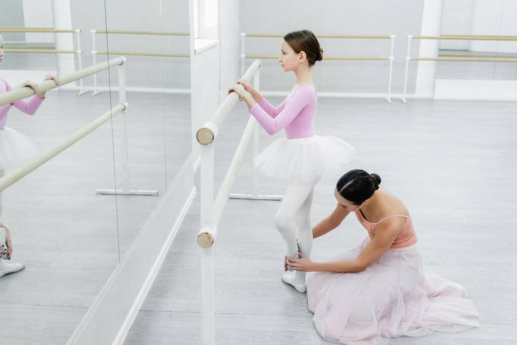 Seitenansicht vom Mädchentraining in der Ballettschule in der Nähe von Spiegeln und Tanzlehrerin - Foto, Bild