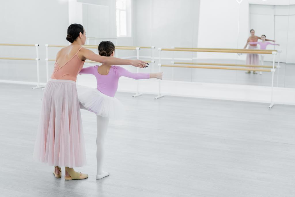 Rückansicht vom Mädchentraining in Ballettschule in der Nähe von Spiegeln und junger Tanzlehrerin - Foto, Bild