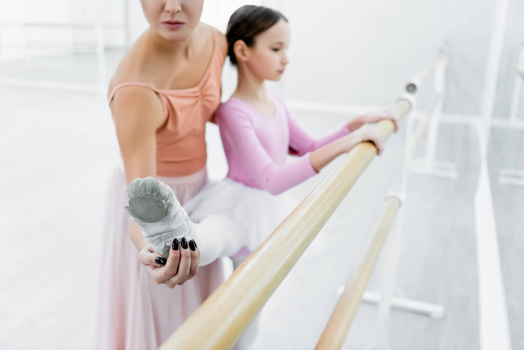ballet teacher helping girl stretching at barre in dance studio, blurred background - Photo, Image