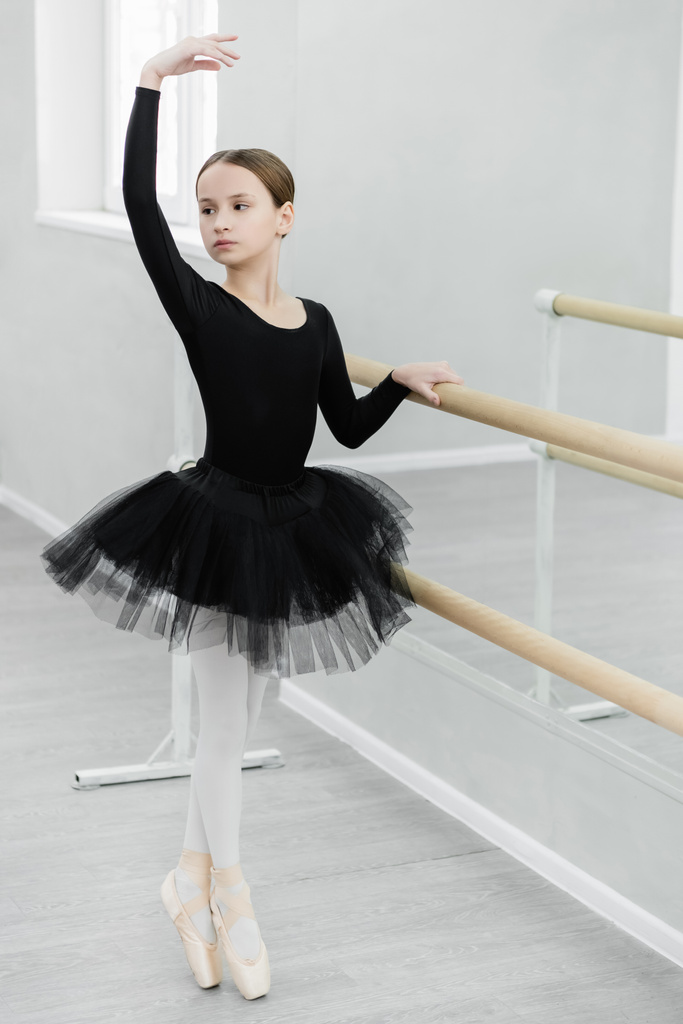 vékony lány fekete tütüben lábujjhegyen áll, miközben a barre táncstúdióban edz - Fotó, kép