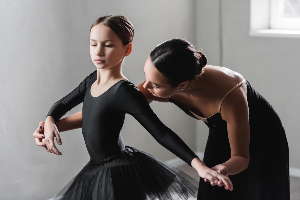 Молодой учитель балета помогает девушке в черной пачке во время урока танцев - Фото, изображение