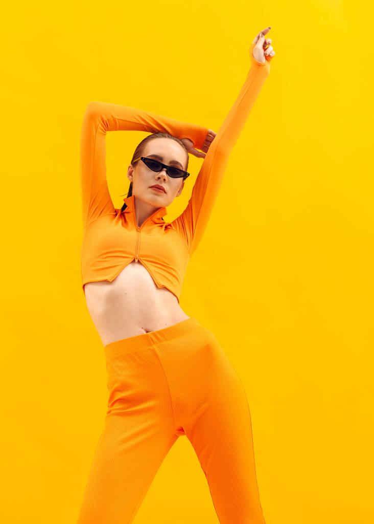 chica elegante en un traje naranja sobre un fondo amarillo en gafas marrones - Foto, Imagen