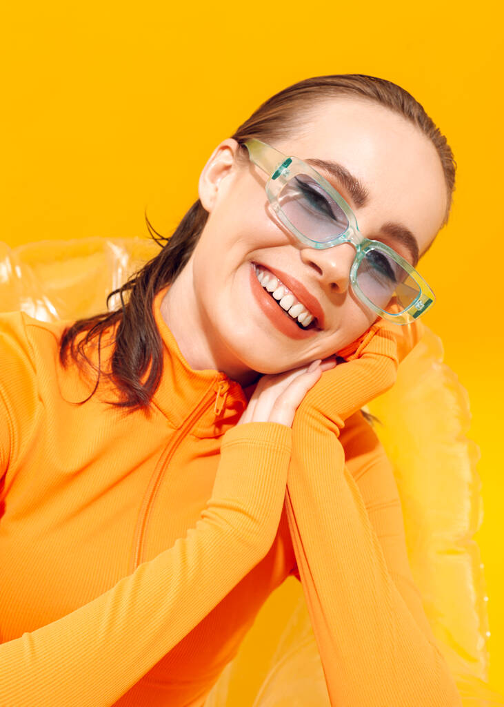 portrét smějící se dívky v modrých brýlích na žlutém pozadí - Fotografie, Obrázek