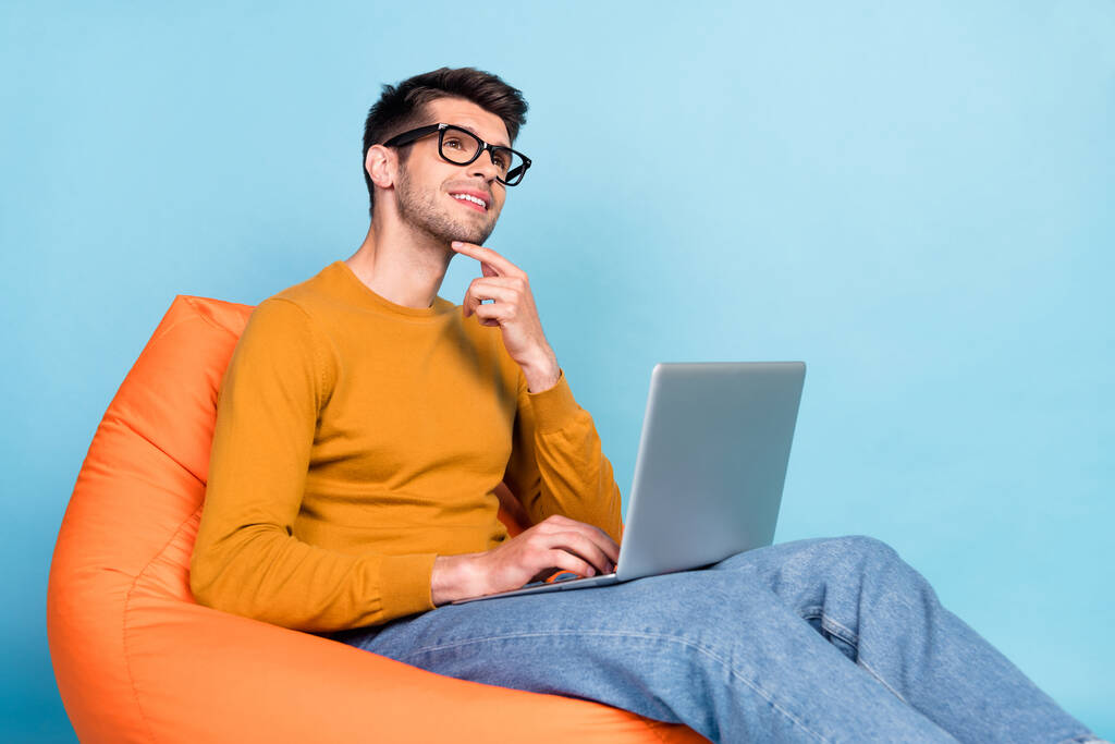 Porträt von attraktiven verträumten fröhlichen Kerl sitzt im Stuhl mit Laptop-Eingabe isoliert über helle blaue Tealfarbe Hintergrund - Foto, Bild