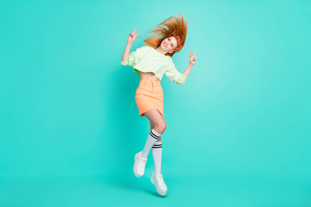 Full size foto van actieve rode haren jonge dame springen show v-teken slijtage trend kleding geïsoleerd op teal kleur achtergrond - Foto, afbeelding