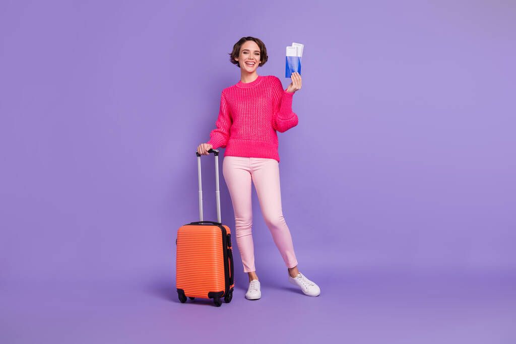 フルサイズの肖像画のかなり陽気な女性ホールドスーツケースパスポートおもちゃの笑顔隔離された紫の色の背景 - 写真・画像