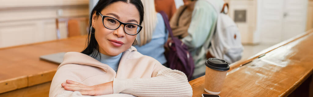 Gözlüklü olgun Asyalı öğrenci üniversiteye gitmek için kahvenin yanındaki kameraya bakıyor.  - Fotoğraf, Görsel