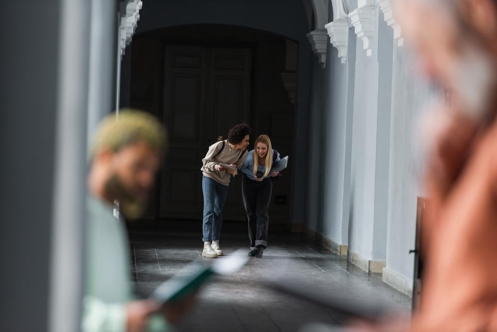 Веселі багатоетнічні студенти з ноутбуком і ноутбуком, що ходять по університетському коридору
  - Фото, зображення