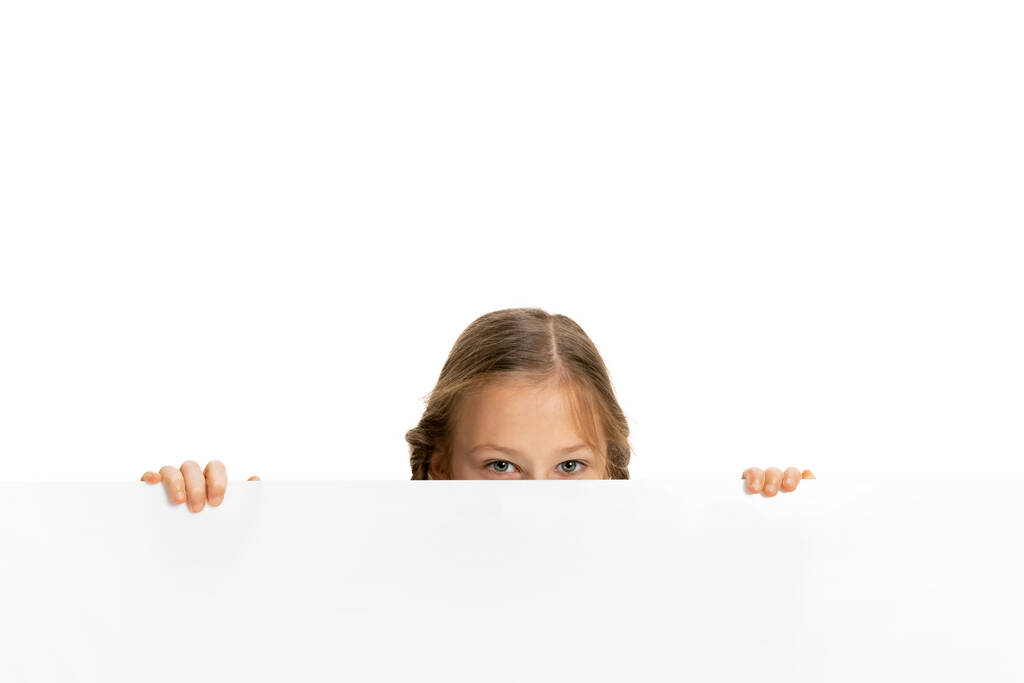Criança engraçada, menina, aluno em roupas de estilo casual espreitando por trás da parede isolada no fundo branco. Conceito de infância, emoções, estudo - Foto, Imagem