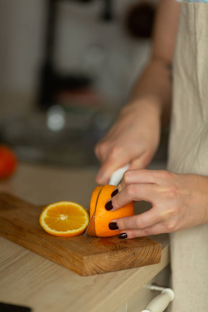 una donna taglia un'arancia in cerchi su un tagliere - Foto, immagini