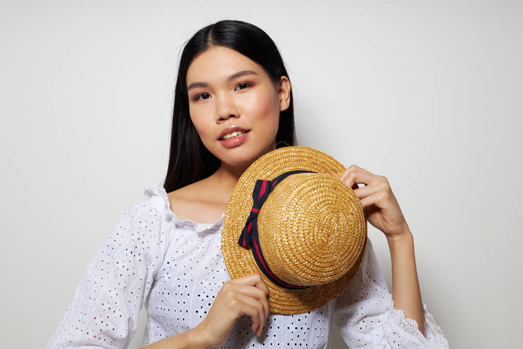 donna con aspetto asiatico cappello in mano posa sorriso luce sfondo inalterato - Foto, immagini