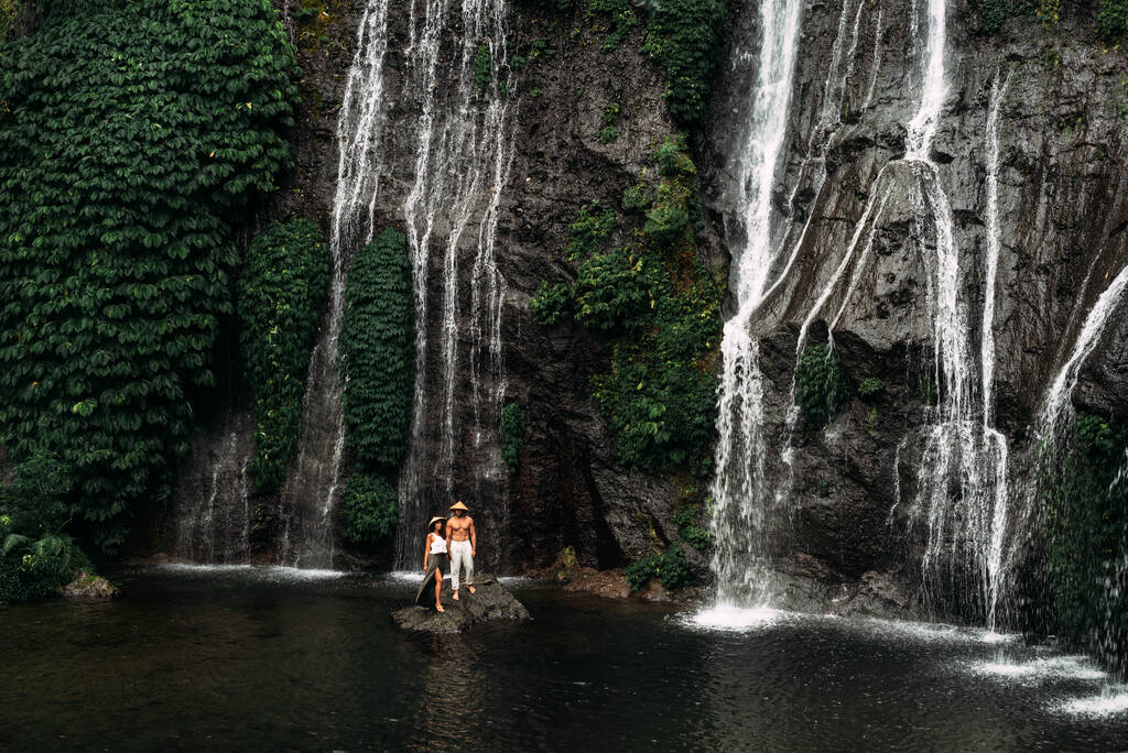 Mężczyzna trzyma za rękę piękną kobietę nad wodospadem. Zakochana para na wodospadzie. Podróż poślubna. Szczęśliwa para na wyspie Bali. Piękna para podróżuje po świecie. Podróż do Indonezji - Zdjęcie, obraz