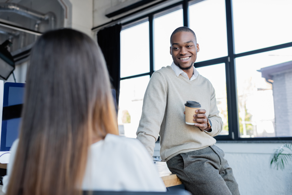усміхнений афроамериканський бізнесмен тримає паперовий стаканчик і розмовляє з розмитим колегою
  - Фото, зображення