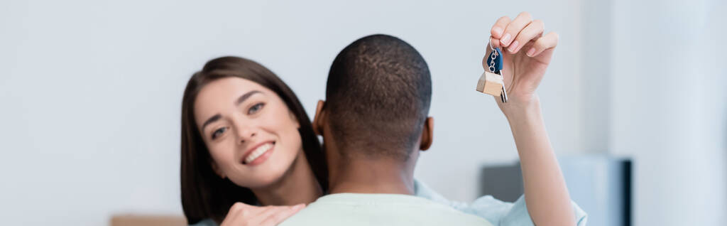 femme heureuse tenant la clé du nouvel appartement tout en étreignant avec petit ami afro-américain, bannière - Photo, image