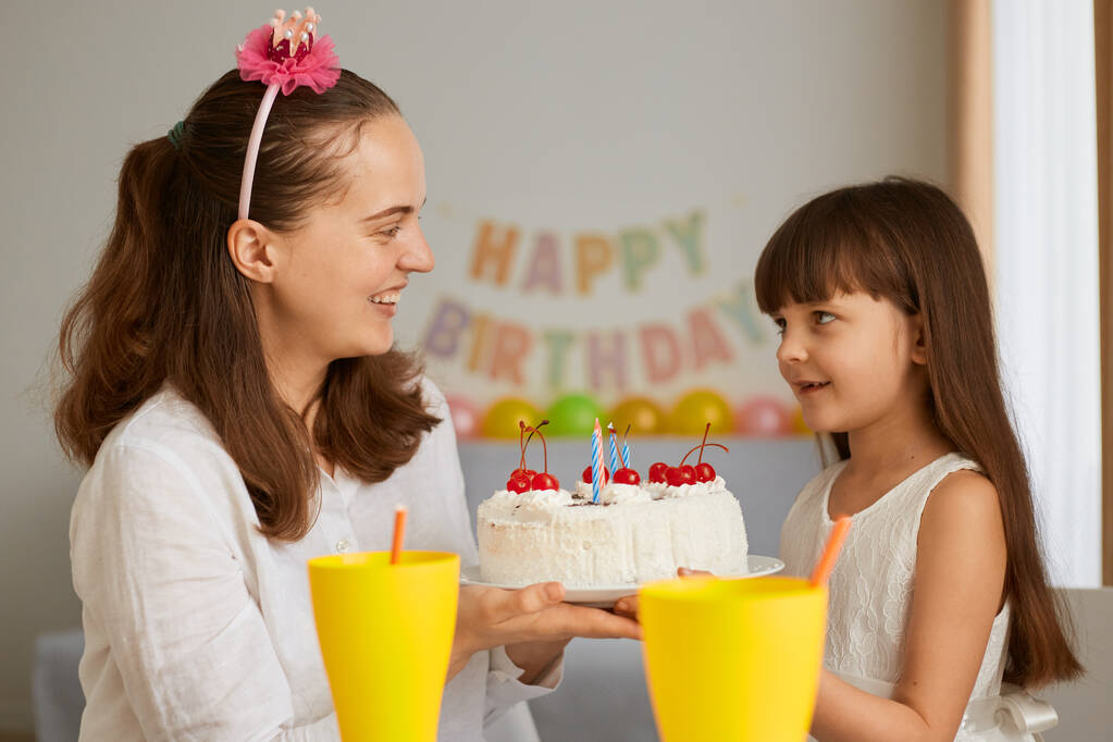 Ritratto di madre e bambina che festeggiano il compleanno con una deliziosa torta per la sua bambina, in attesa di soffiare le candele sorridenti, guardandosi con amore e gentilezza. - Foto, immagini