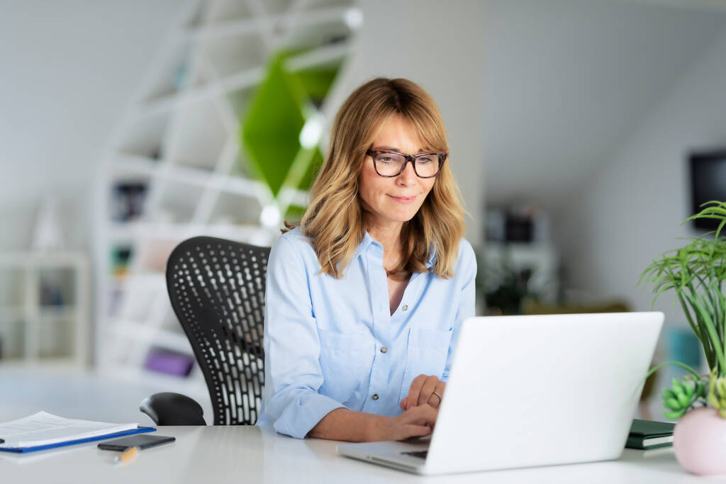 Уверенная деловая женщина сидит в офисе и работает на ноутбуке. - Фото, изображение
