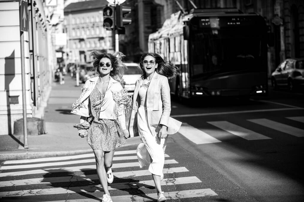 Salido amigos niñas corriendo en crosswalk, pasando un gran tiempo juntos en verano calle ciudad. - Foto, imagen