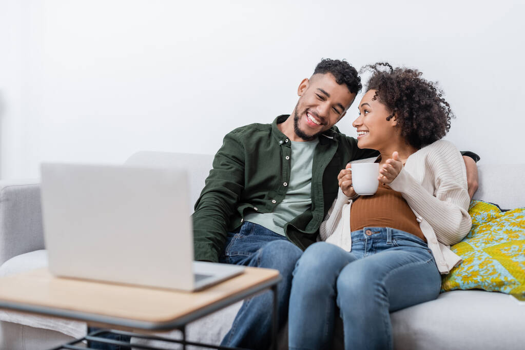 счастливый африканский американский муж и беременная жена смотрят фильм на ноутбуке - Фото, изображение