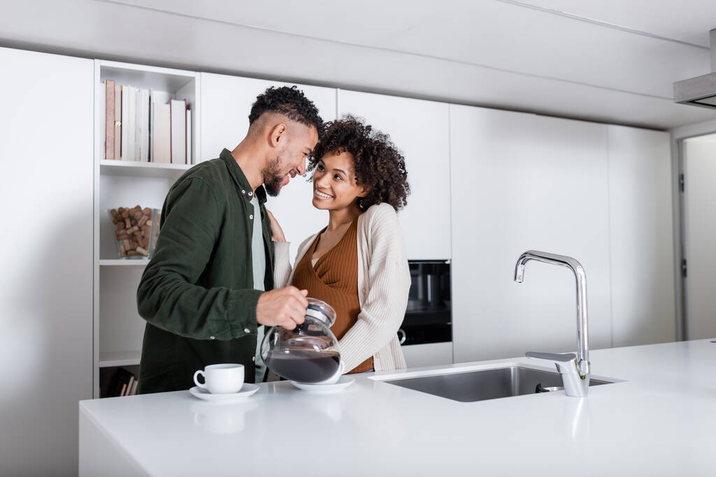 happy african american man pouring coffee near cheerful pregnant wife  - Photo, Image