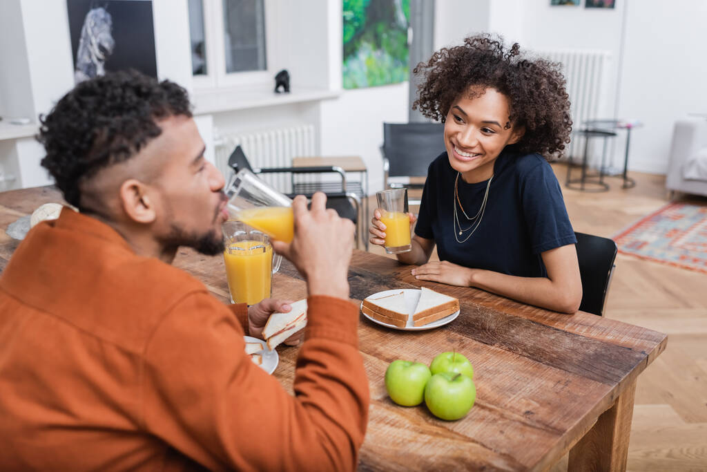 幸せなアフリカ系アメリカ人女性持っています昼食とともにぼやけたボーイフレンド飲みオレンジジュース  - 写真・画像