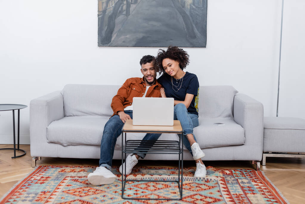 Modern dairede dizüstü bilgisayardan film izlerken gülümseyen genç Afrikalı Amerikalı çift.   - Fotoğraf, Görsel