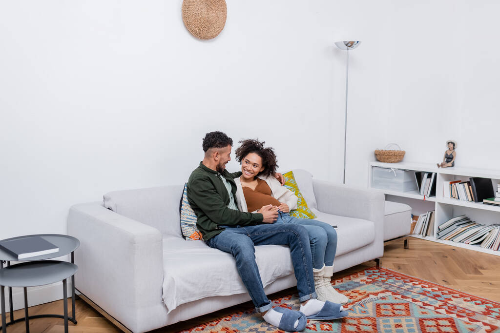 mulher americana africana feliz e grávida sentada com marido feliz no sofá  - Foto, Imagem