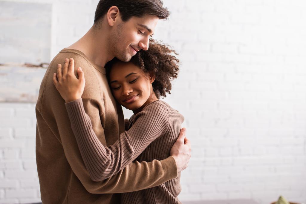 Sorrindo casal multiétnico abraçando na sala de estar  - Foto, Imagem