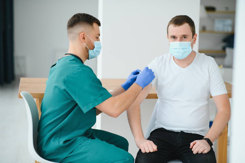 Medizin, Impfung und Gesundheitskonzept - Arzt mit Gesichtsschutzmaske zum Schutz vor Viruserkrankungen mit Injektion von Impfstoff an männlichen Patienten - Foto, Bild