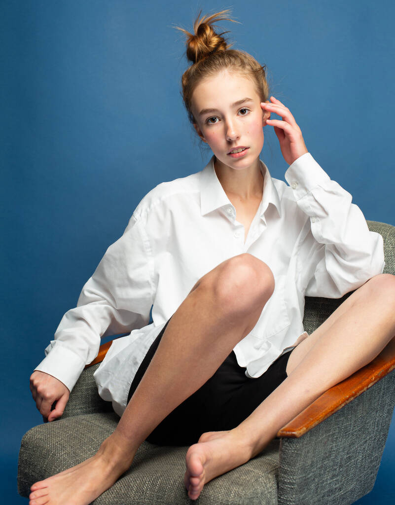 Kırmızı saçlı, beyaz tenli, mavi tenli, sandalyede bacaklarıyla oturan Avrupalı bir kız. - Fotoğraf, Görsel