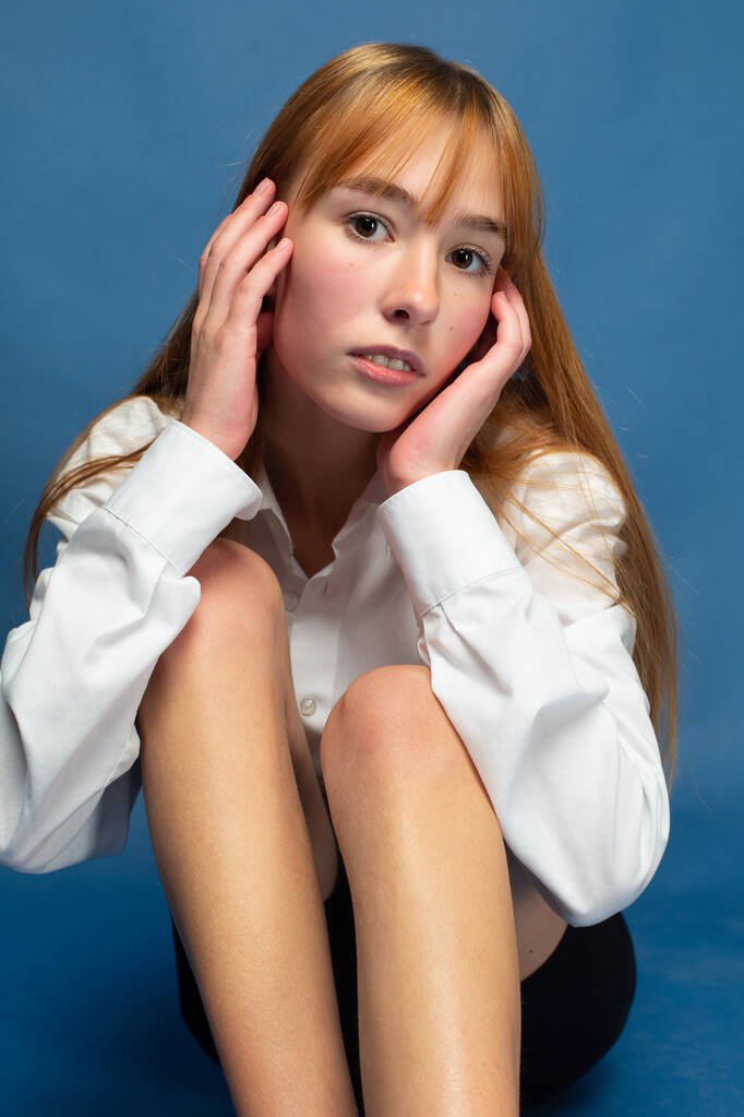 Jong meisje met rood haar en witte huid geïsoleerd op blauw met handen in de buurt van haar gezicht - Foto, afbeelding