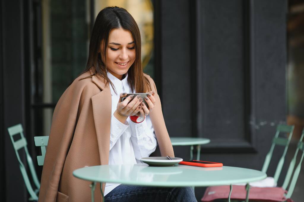 Портрет молодой красивой женщины, сидящей в кафе на открытом воздухе и пьющей кофе - Фото, изображение