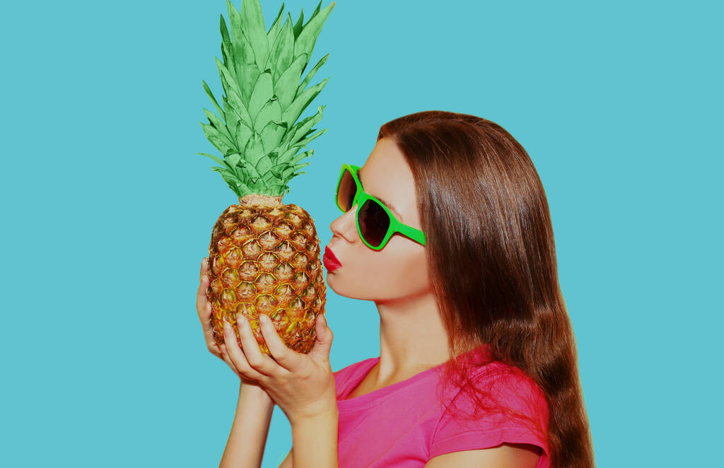 Portret van een jonge vrouw met ananas in een zonnebril op een blauwe achtergrond - Foto, afbeelding