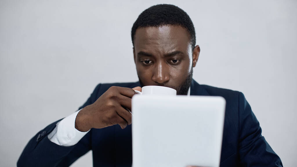 Afrikanischer amerikanischer Geschäftsmann nutzt digitales Tablet beim Kaffeetrinken isoliert auf grau - Foto, Bild