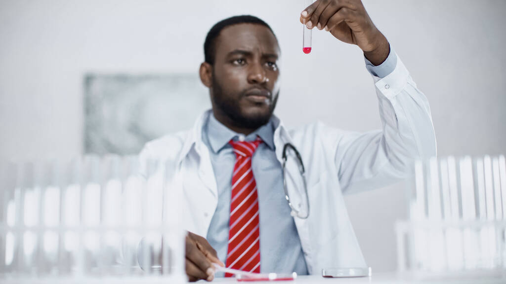 parrakas afrikkalainen tiedemies katselee punaista nestettä koeputkessa  - Valokuva, kuva